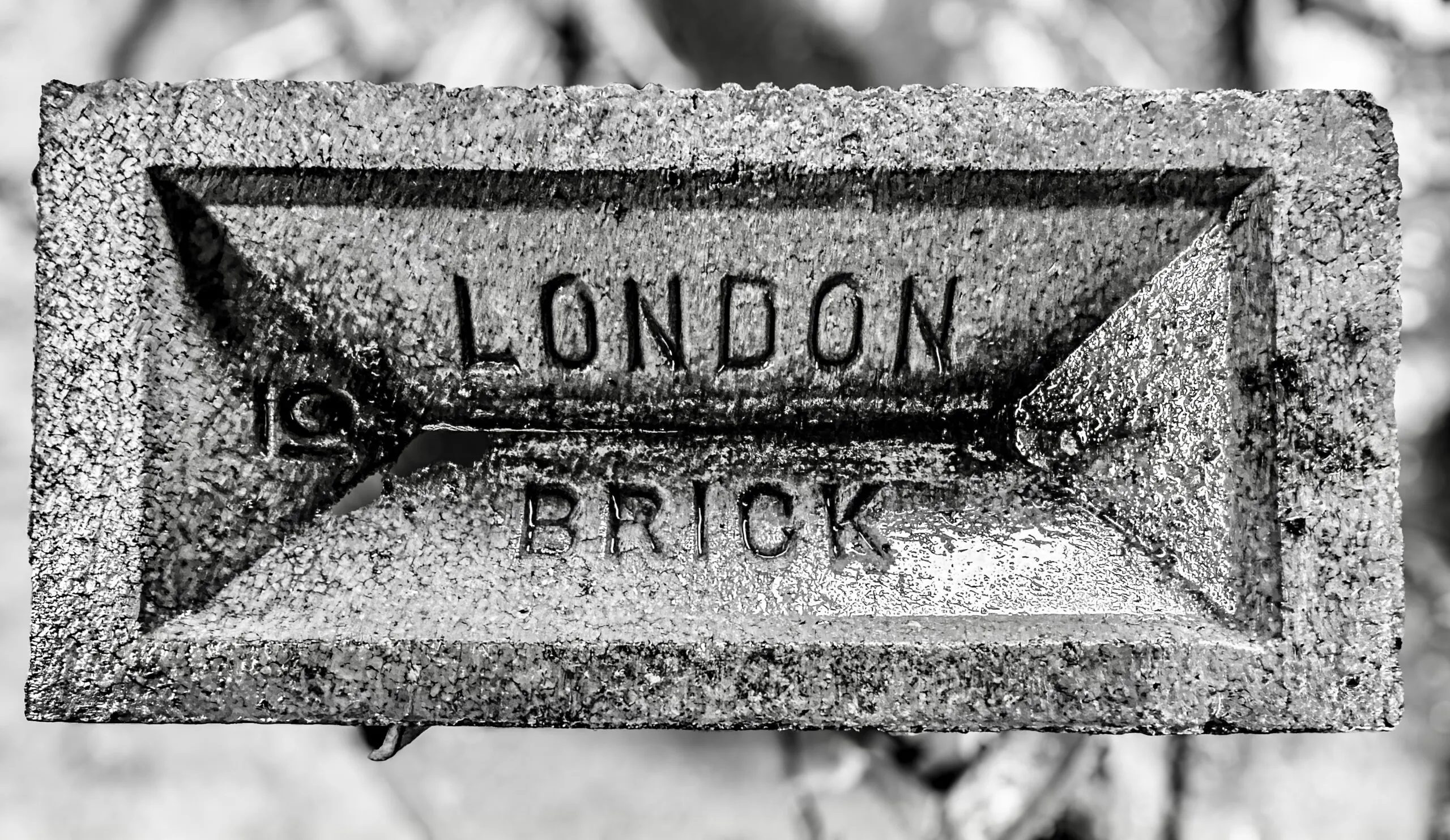 A black and white close-up of a brick stamped with the words 'LONDON BRICK' in a recessed frog