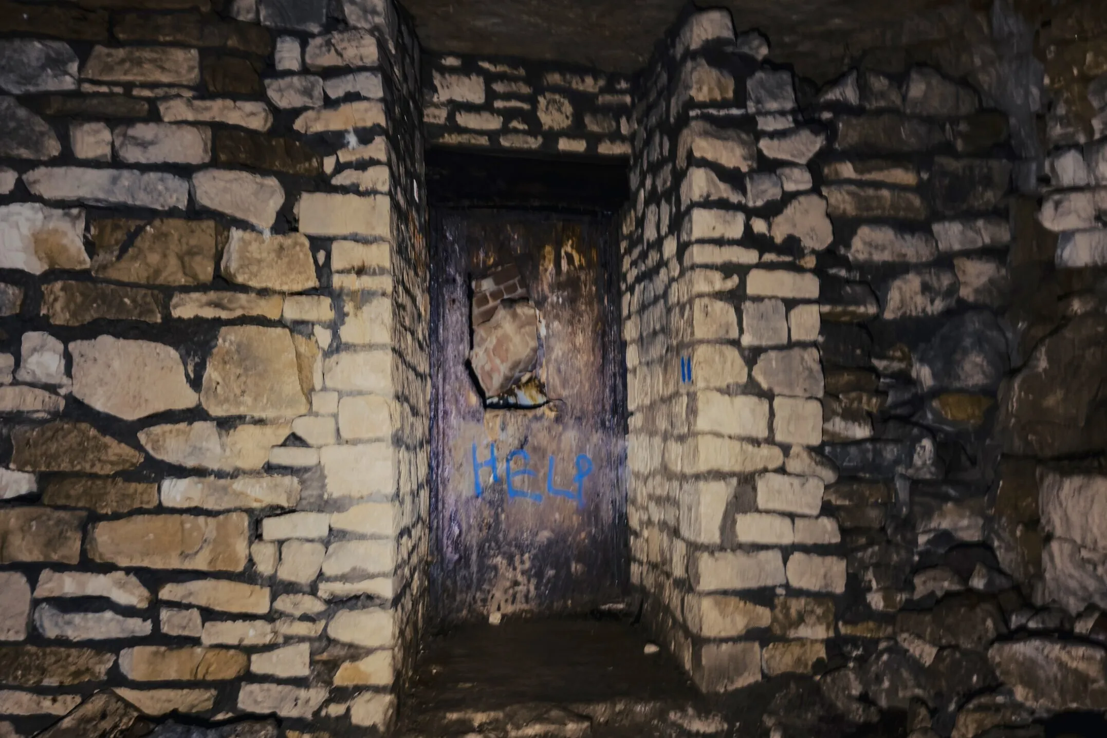 A drystone-walled doorway deep in the mine, the word 'HELP' sprayed in blue on the blocking beyond