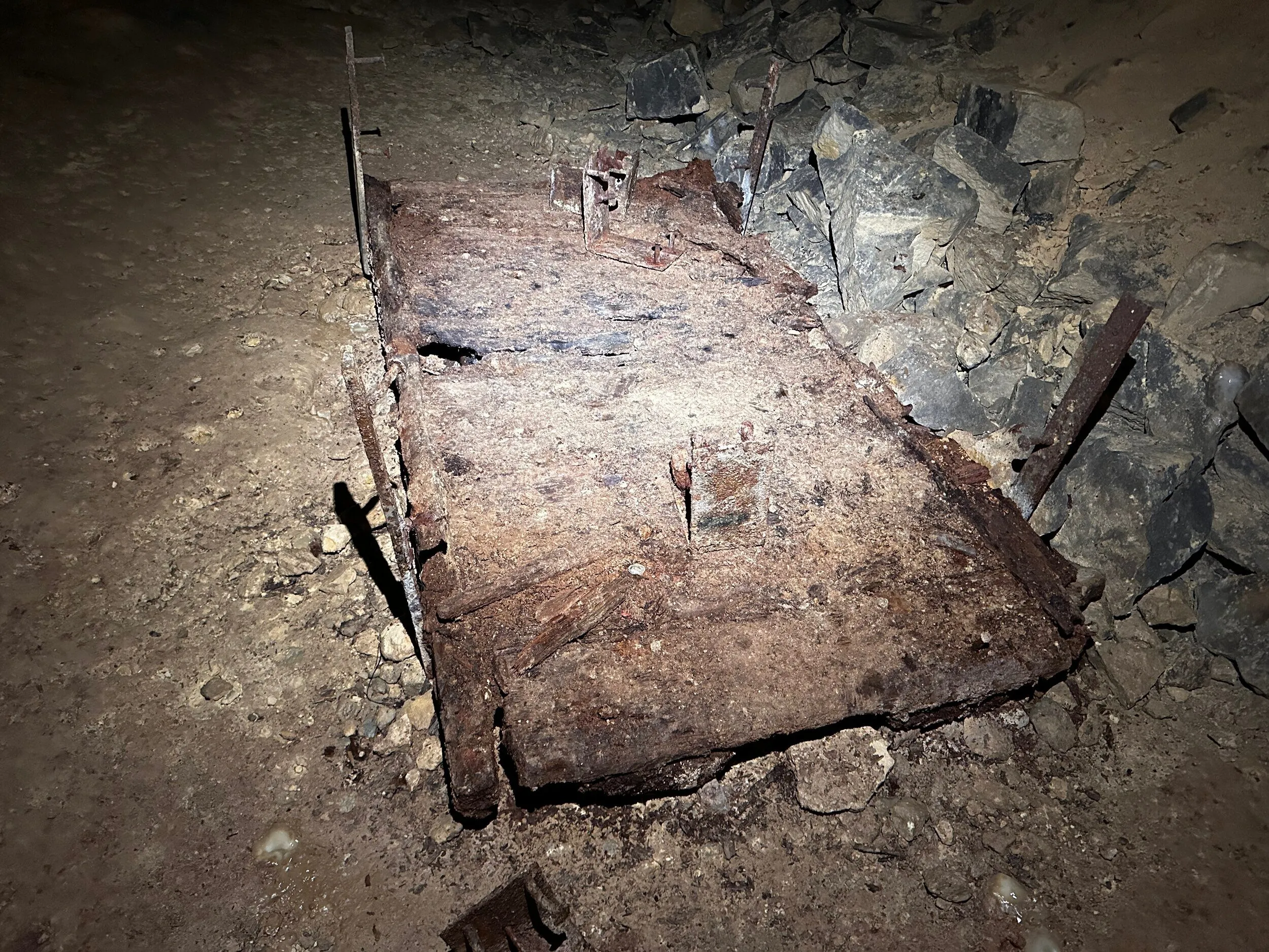 The rusted iron frame of a mine trolley lying flat on the passage floor among fallen stone